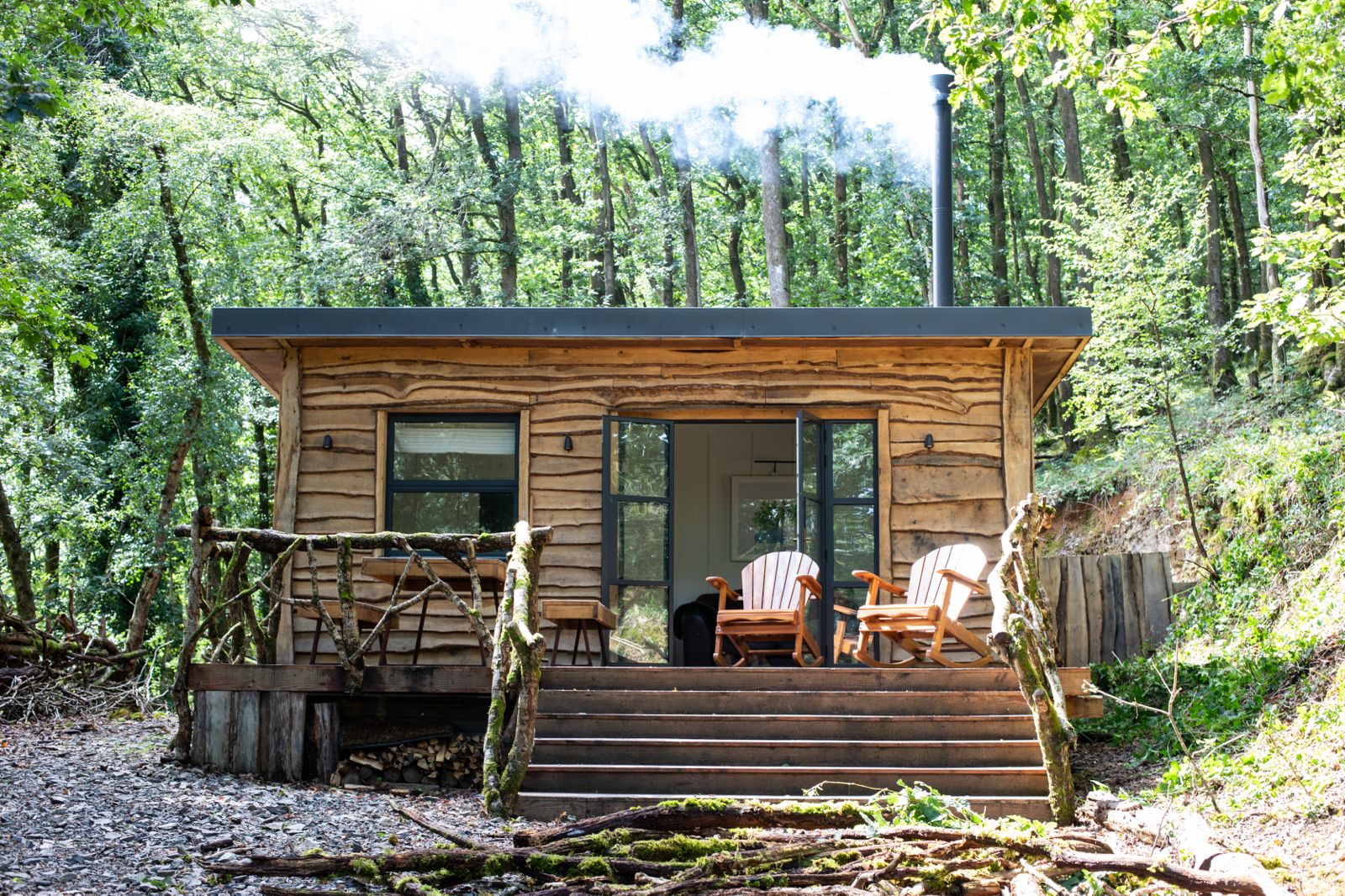Handcrafted timber-clad woodland cabin by Brecon Oak featuring log burner chimney smoke and rustic porch seating