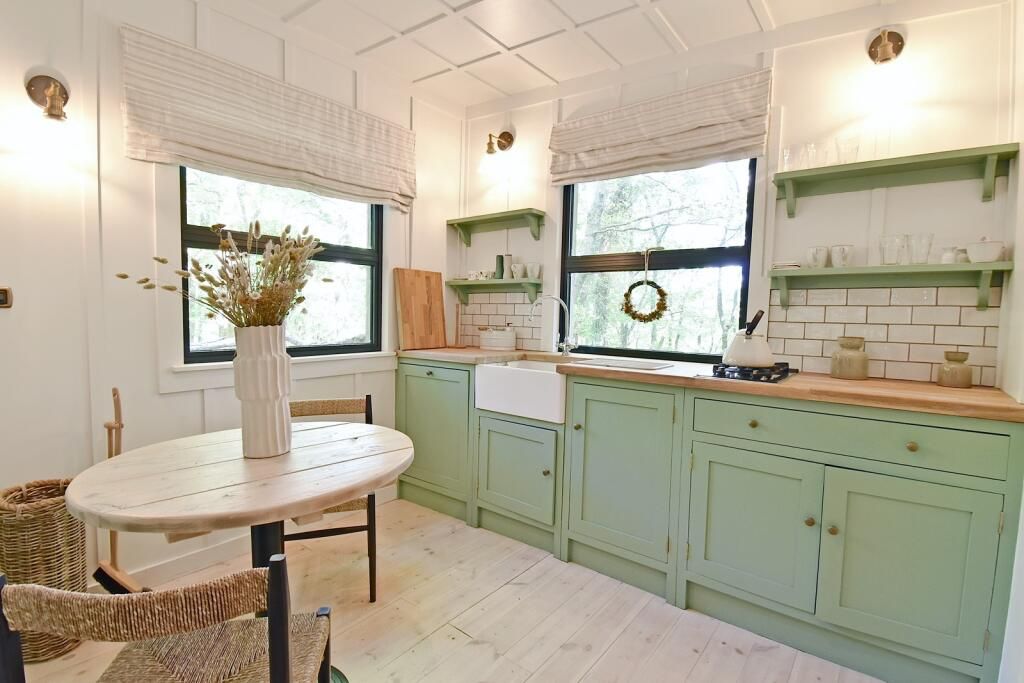 Bespoke sage green kitchen inside the off-grid cabin featuring solid wood worktops, Belfast sink, and panelled walls