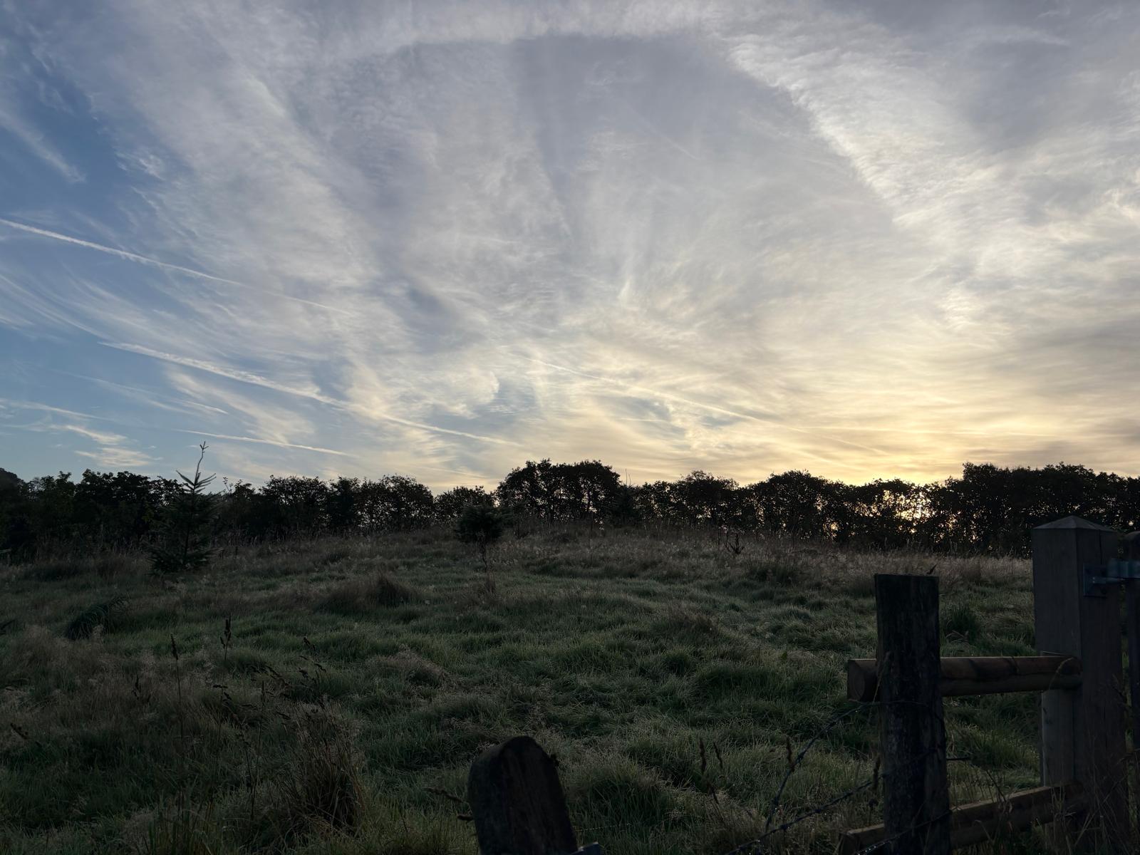 Rustic wooden estate fencing before rolling meadow and autumn sunrise silhouette